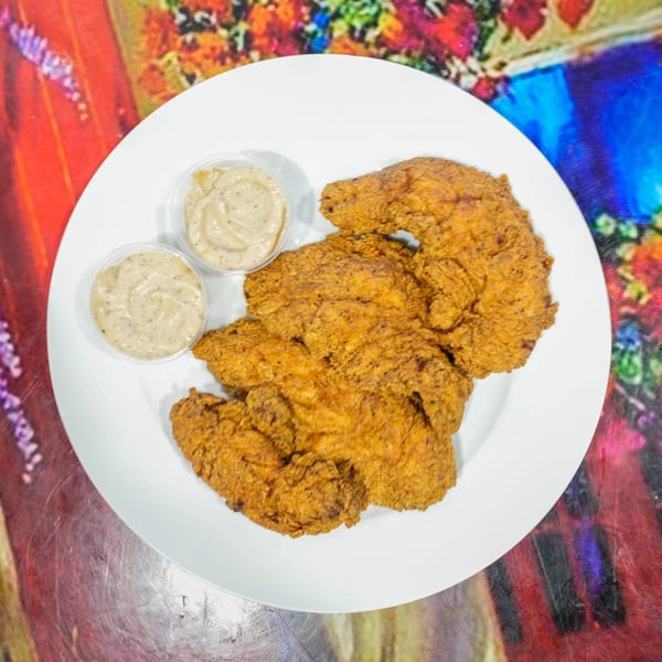 Crispy fried chicken cutlets with two small cups of dipping sauce on a white plate.