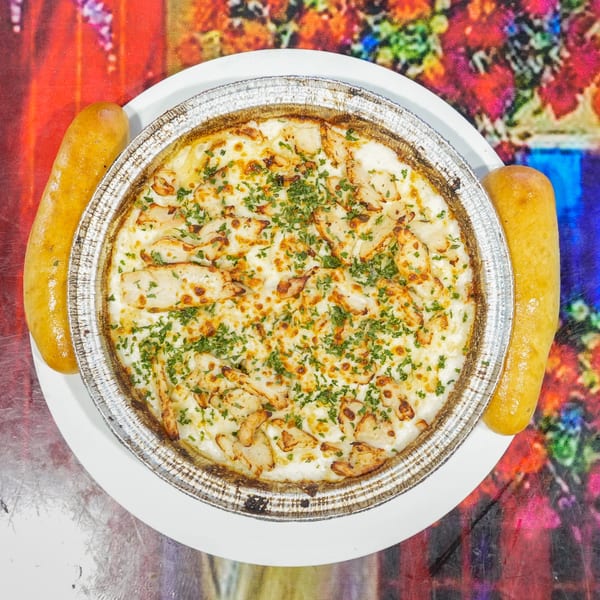 Cheesy chicken dip with parsley in a foil pan, flanked by two breadsticks on a colorful background.