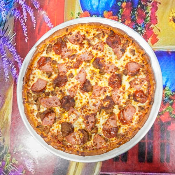 ELE PIZZA's meat lover's pizza, topped with pepperoni, sausage, and ham, on a colorful floral tablecloth.