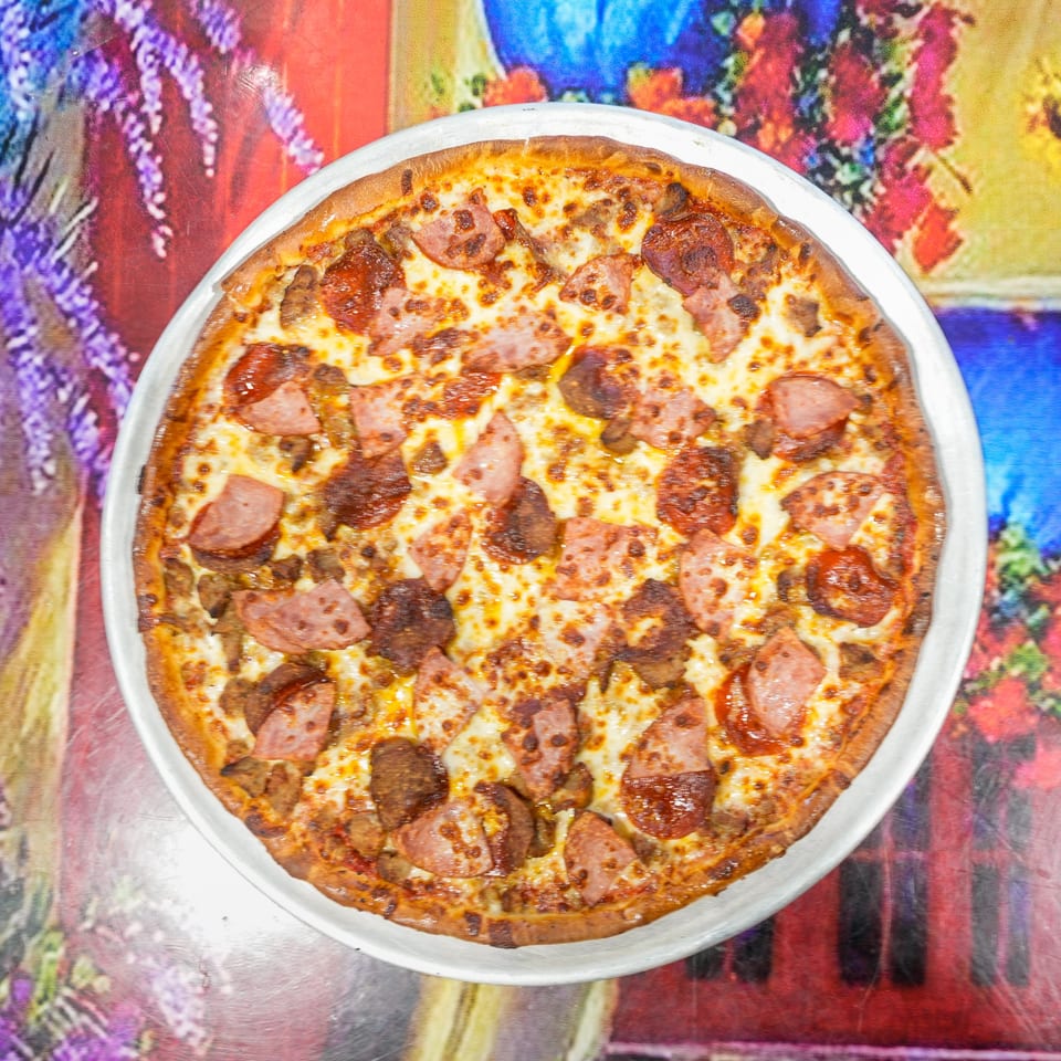 ELE PIZZA's meat lover's pizza, topped with pepperoni, sausage, and ham, on a colorful floral tablecloth.