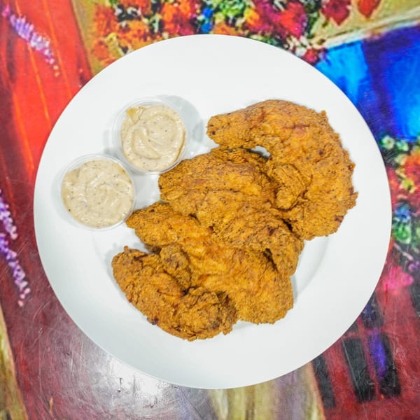 Crispy fried chicken tenders with two cups of dipping sauce on a white plate.